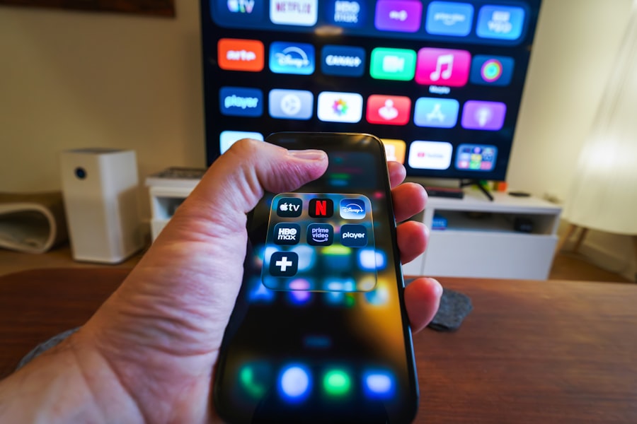 Hand holding a smartphone displaying streaming service applications in front of a large smart TV — IPTV Smarters Pro on Firestick and PC